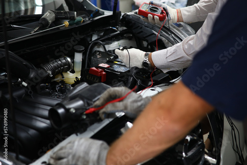 Professional auto mechanic works in a car service and tests operation of engine with tester