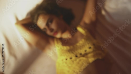 Brunette girl with red lips and yellow outfit lying down and looking towards the camera. Blurred overhead shot from above. photo