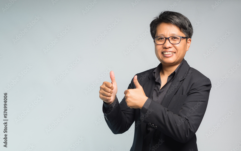 Portrait of a businesswoman with short black hair in a suit hands showing thumbs up while standing on a gray background Portrait of a businesswoman with short black hair in a suit hands showing thumbs up while standing on a gray background