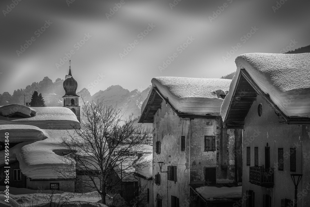 Black and white view of houses in small Dolomite village with snow-covered roofs. Val di Zoldo, Dolomites, Italy