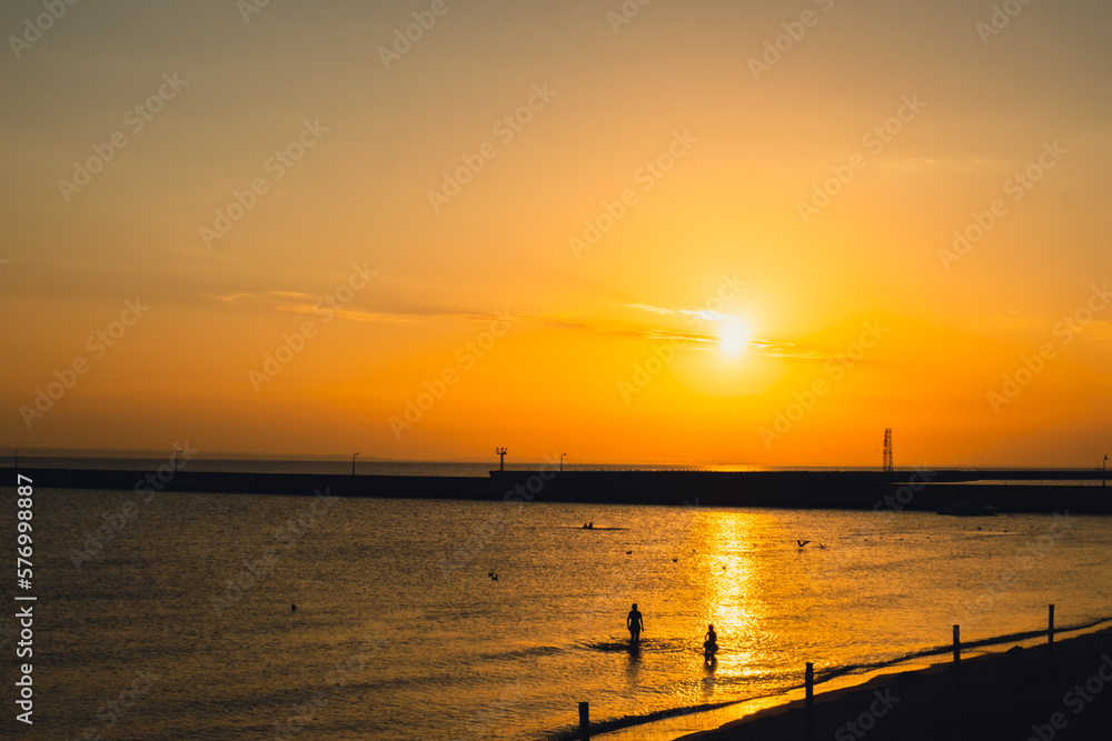 Silhouette of people enjoying sea and summer days. Reflection of sunlight over sea surface at sunset. Orange and gold blue sky. Scenic Gold sea. Dramatic Yellow sun coming out of the sea. Majestic