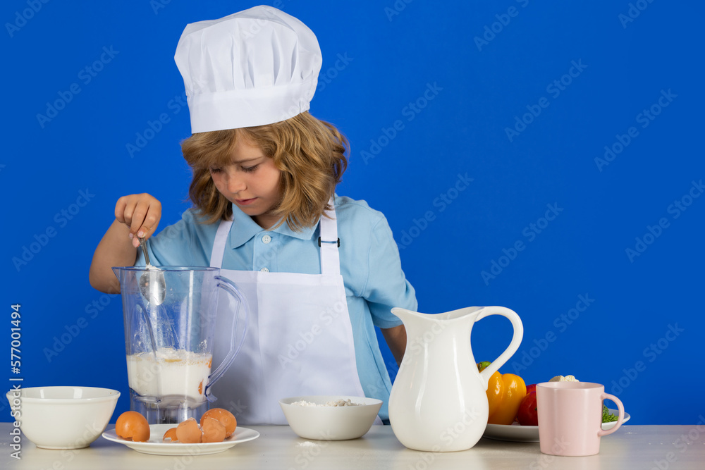 Child wearing cooker uniform and chef hat preparing vegetables on kitchen, studio portrait. Cooking, culinary and kids food concept. Child wearing cooker uniform and chef hat preparing vegetables on kitchen, studio portrait. Cooking, culinary and kids food concept.
