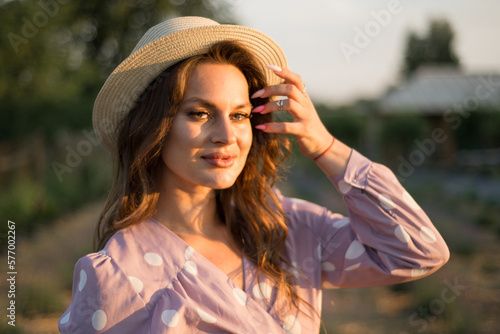 Portrait of young sexy woman stands in lavender field and holds hat.