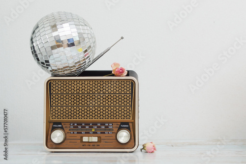 The vintage style of the old retro radio on which the round disco ball lies on the table against the background of the white wall, the sluggish roses are randomly scattered, and copy the space.