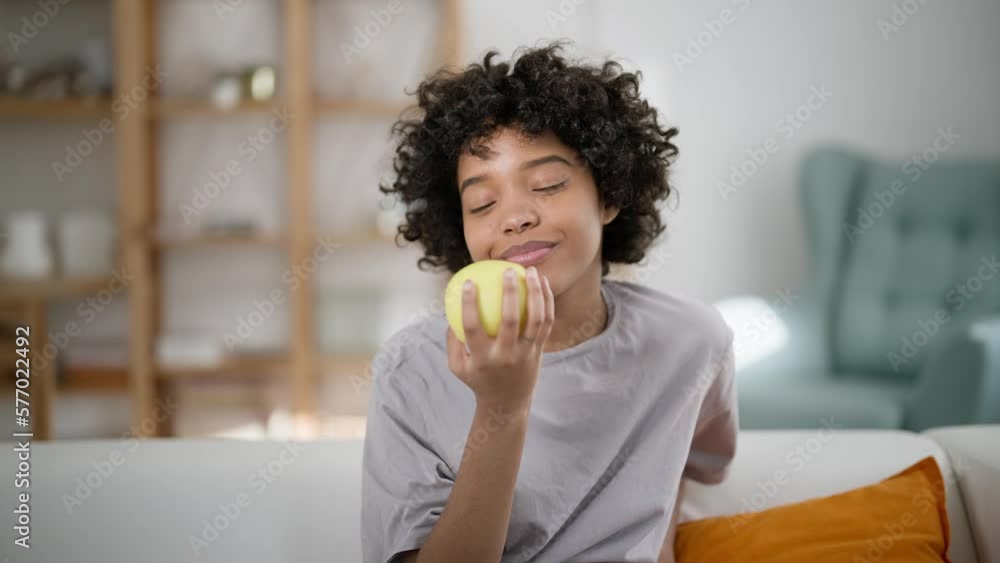Attractive cute young woman eating apple. Portrait of happy african american girl biting and eating ripe green apple, looking at camera at home interior. Concept enjoy healthy diet and lifestyle. Attractive cute young woman eating apple. Portrait of happy african american girl biting and eating ripe green apple, looking at camera at home interior. Concept enjoy healthy diet and lifestyle.