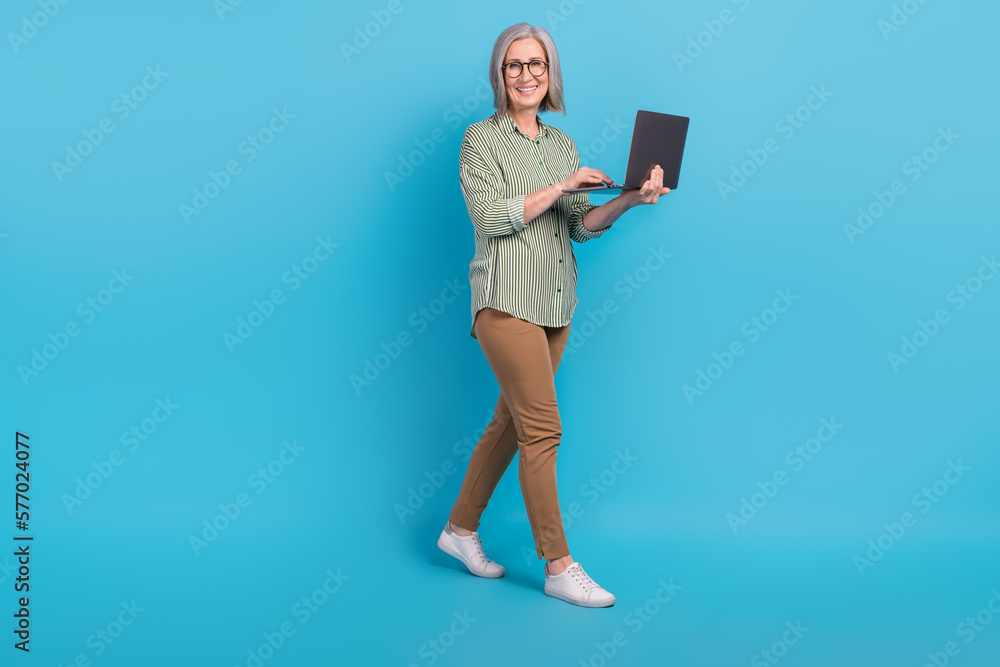Full body length photo cadre of successful business woman walking with laptop freelancer online communication isolated on blue color background Full body length photo cadre of successful business woman walking with laptop freelancer online communication isolated on blue color background