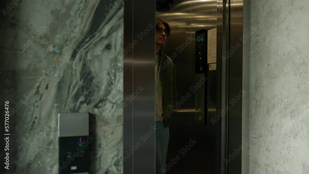 Confident brunet Asian man in headphones going down in the elevator in the office Confident brunet Asian man in headphones going down in the elevator in the office