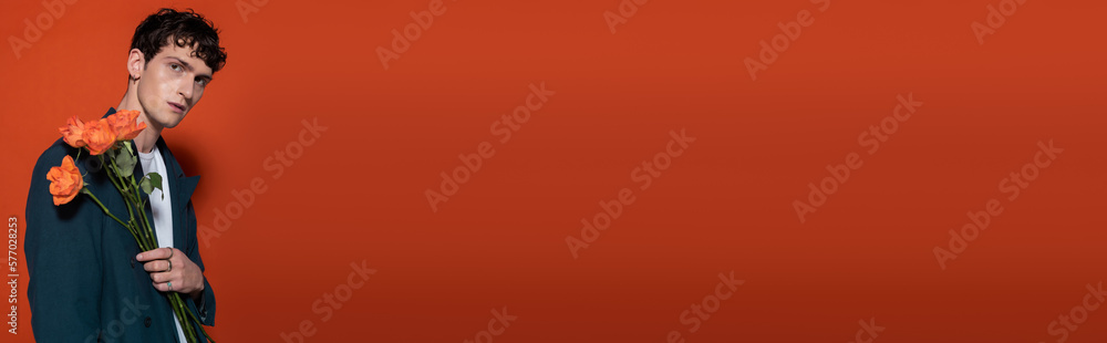 Trendy man in blue blazer holding orange flowers for 8 march on red background, banner. Trendy man in blue blazer holding orange flowers for 8 march on red background, banner.