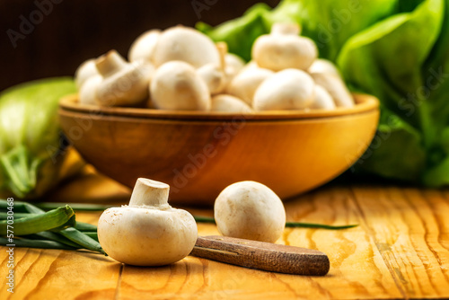 Fresh white mushrooms champignon in brown wooden bowl on wood table background