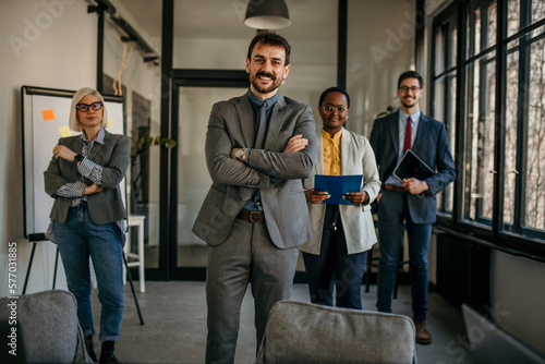 Portrait of handsome smiling businessman with his colleagues. Multi-ethnic group of business persons standing in modern office. Successful team leader and his team in the background