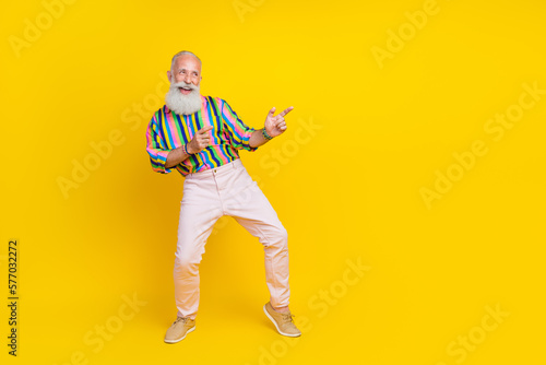 Full length photo of pretty cool guy dressed striped shirt looking pointing empty space isolated yellow color background