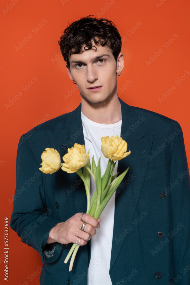 Portrait of stylish brunette man holding yellow tulips isolated on red. Portrait of stylish brunette man holding yellow tulips isolated on red.