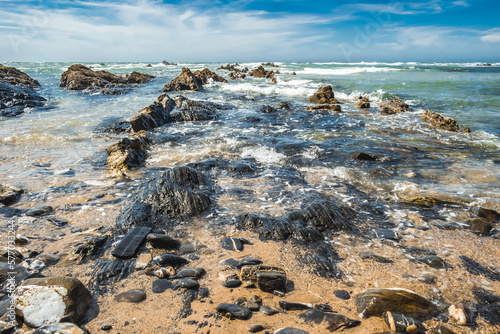 Black and wet rocks by the Atlantic Ocean and sand at Almograve beach in Costa Vicentina, PORTUGAL