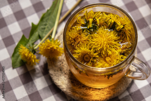 Dandelion flower healthy tea in glass cup on table. Herbal medicine Delicious tisane tea from with fresh yellow blossom dandelion flowers inside tea cup. Green clearing infusion Wildflowers Eco