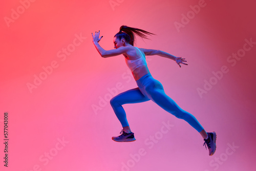 Dynamic portrait of young active girl, running athlete in motion, training over pink studio background in neon light. Concept of sportive lifestyle, health, endurance, action and motion. Ad
