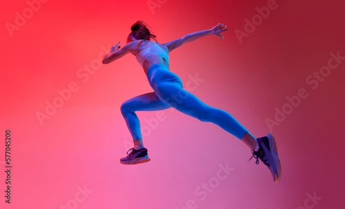 Bottom view. Young female professional athlete, runner in motion, training over pink studio background in neon light. Concept of sportive lifestyle, health, endurance, action and motion. Ad