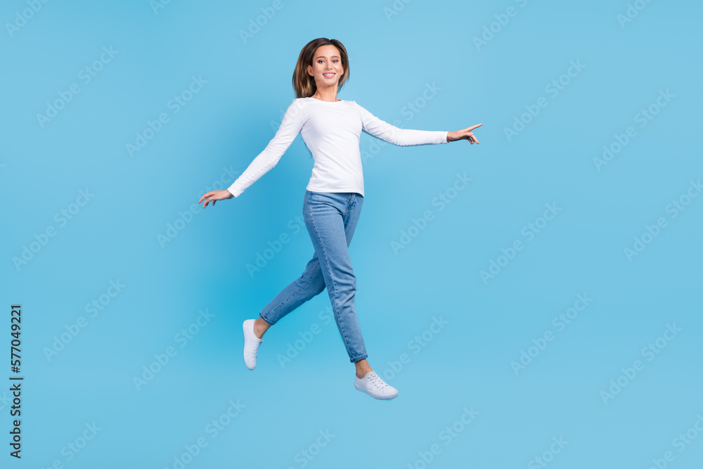 Full length photo of adorable charming lady dressed white shirt walking jumping high emtpy space isolated blue color background