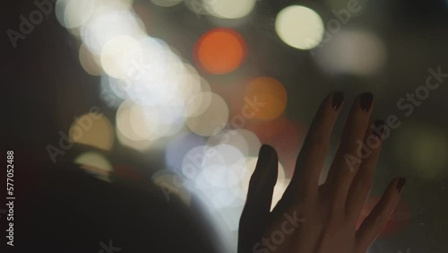 View of tender woman hand touching window glass, watching night city lights being indoors. Car lights reflected in the glass, bokeh, soft focus. Missing and dreaming about something. 4k footage