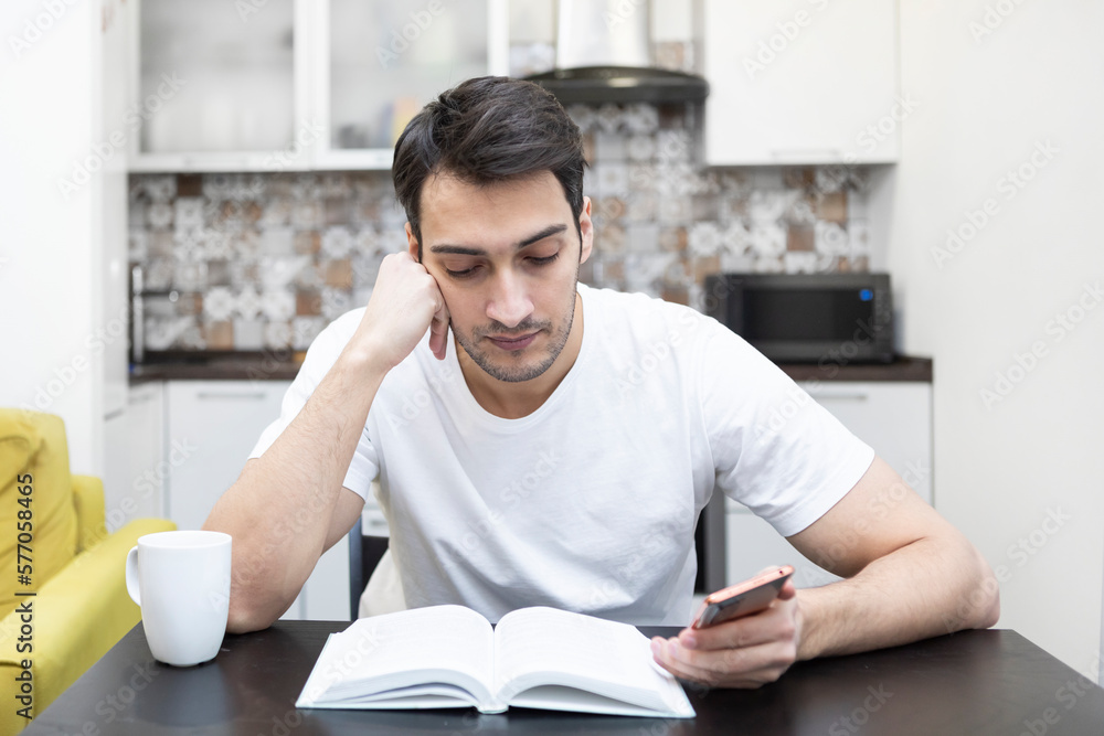 Young handsome man reading book and drinking tea in the kitchen Young handsome man reading book and drinking tea in the kitchen