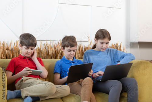 Portrait of modern children sitting on the couch and looking at their gadget. Gadget addiction concept