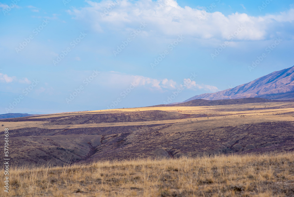 Unusual mountain landscape with bright cloudy skies. Autumn in remote foothills in northern China. Dry grassy and hills. Natural background. Exploration of new places, travel to remote locations.