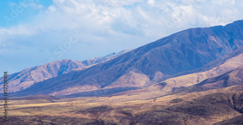 Unusual mountain landscape with bright cloudy skies. Autumn in remote foothills in northern China. Dry grassy and hills. Natural background. Exploration of new places, travel to remote locations.