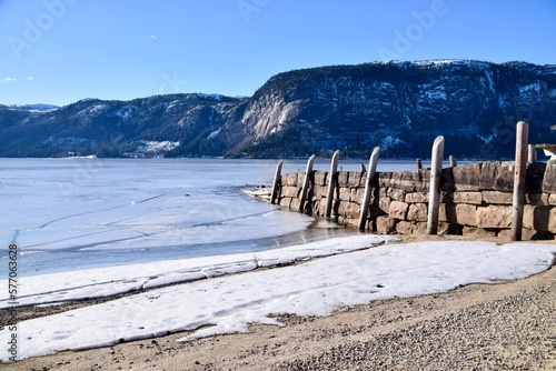 Wood and stone pier at Bygland  Norway. Mountains behind and snow on the beach. Frozen Lake. Blue skies. 