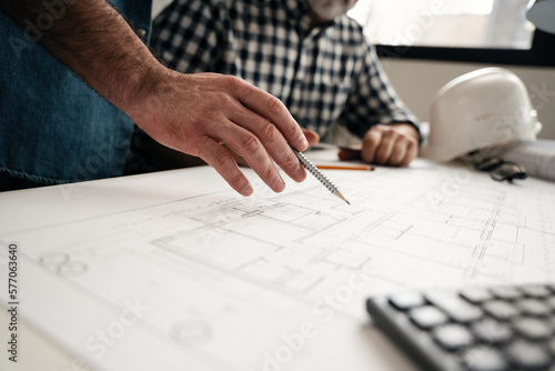 Architects engineer discussing at the table with blueprint - Closeup on hands and project print. © opolja
