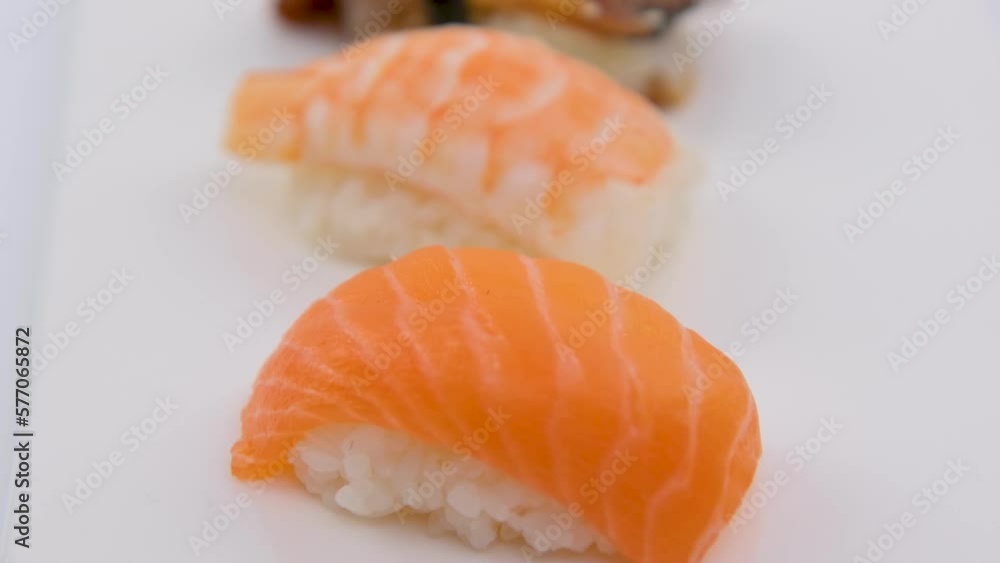 Chopsticks takes sushi with escolar from assorted sushi on a black plate on dark background. Minimal concept. High quality 4k footage Chopsticks takes sushi with escolar from assorted sushi on a black plate on dark background. Minimal concept. High quality 4k footage