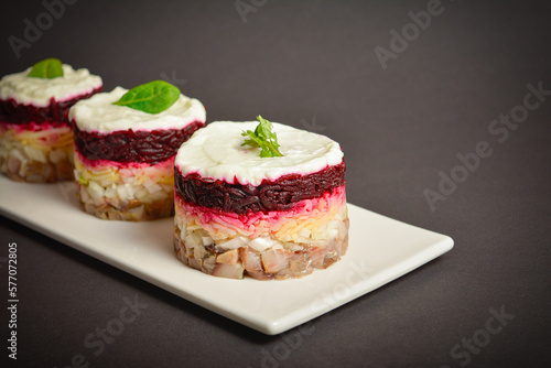 Side view of holiday layered fish salad Herring under fur coat served in culinary rings. serving size of Eastern Europe salad with beetroot, potato, onion, fish and mayonnaise with towel on background