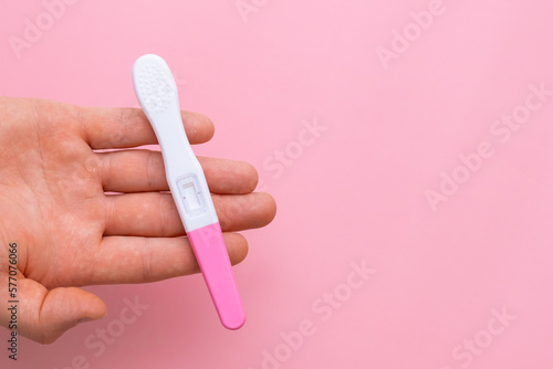 Man hand holding a pregnancy test on the pink background with copy space