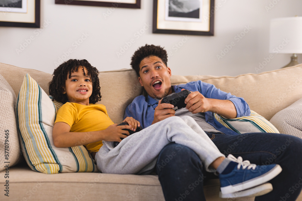 Cheerful hispanic father and son playing video games while sitting on sofa in living room Cheerful hispanic father and son playing video games while sitting on sofa in living room