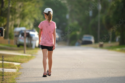 Rear view of confident young child girl walking along the sunny alley. Active lifestyle on summer holidays