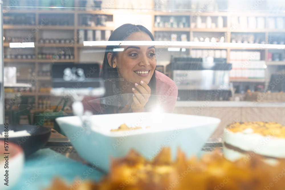 Smiling young caucasian female customer seen through food cabinet glass at coffee shop Smiling young caucasian female customer seen through food cabinet glass at coffee shop