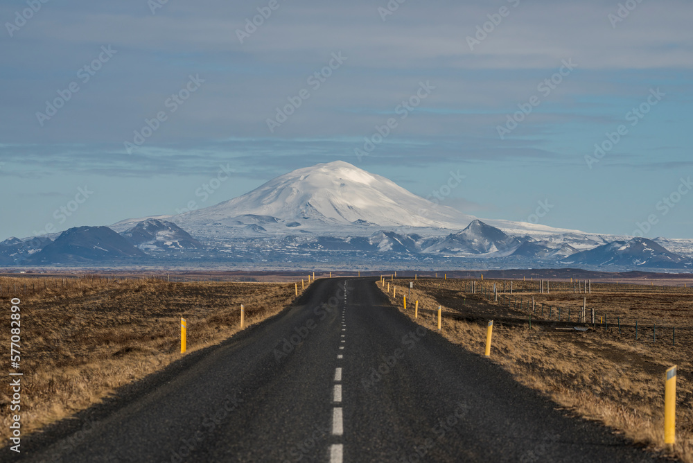 Empty asphalt road in Iceland with a big snowy mountain in the background.