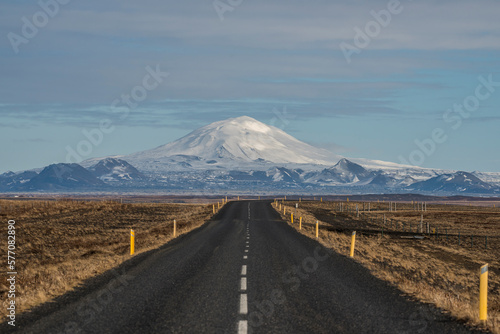 Empty asphalt road in Iceland with a big snowy mountain in the background.