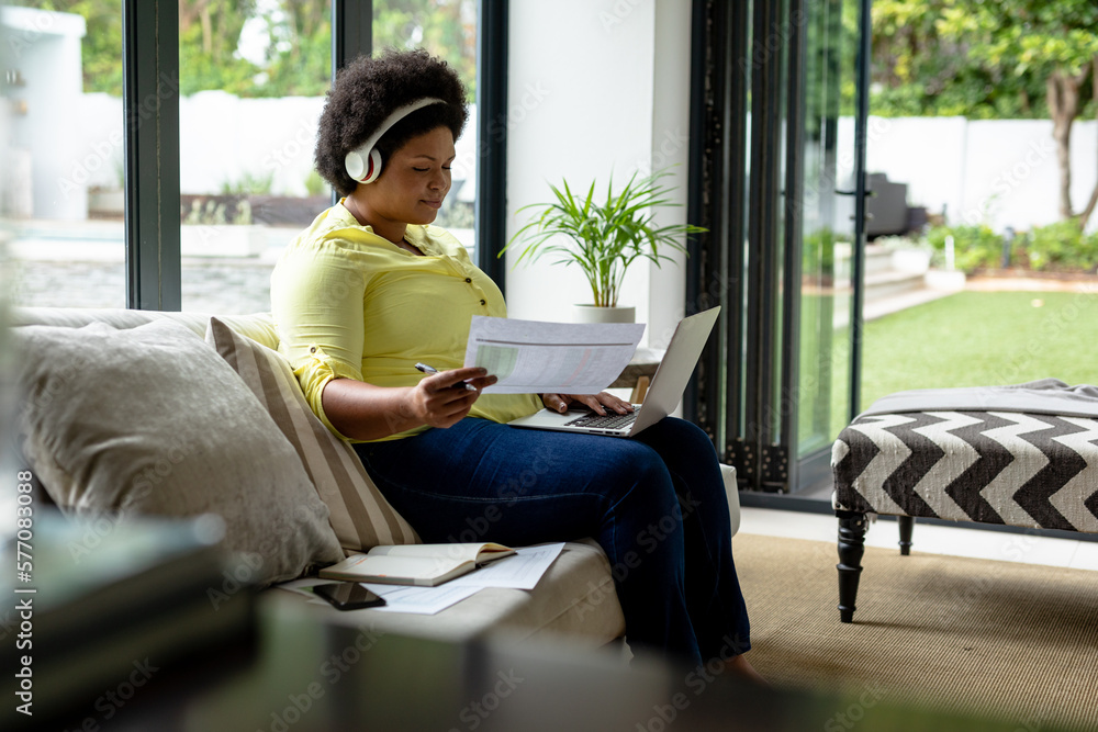 African american mid adult businesswoman holding document while working on laptop at home African american mid adult businesswoman holding document while working on laptop at home