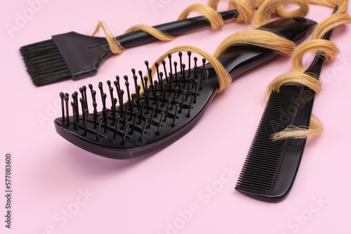 Professional hairdresser's tools. Black combs, brush for coloring hair on a pink background with blond curls. Providing hairdressing services. Close-up