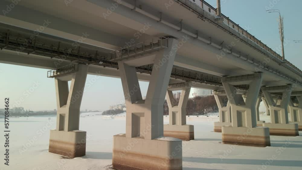 View of the pillars of the road bridge across the river in winter. Footage from a drone flying under the bridge on a sunny winter day. 4k View of the pillars of the road bridge across the river in winter. Footage from a drone flying under the bridge on a sunny winter day. 4k