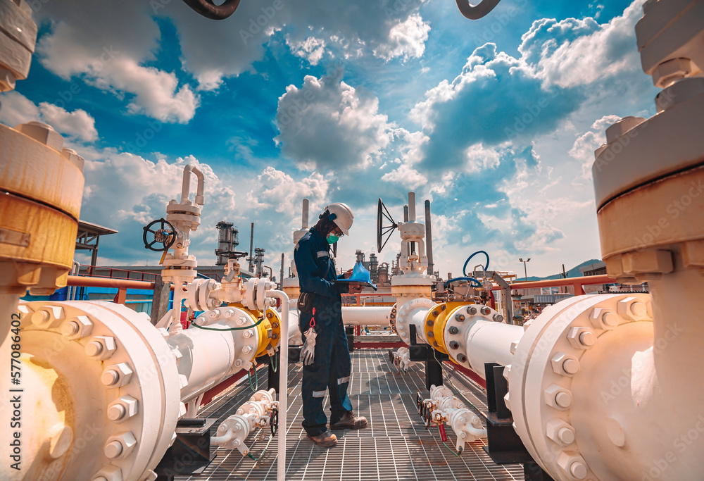 © chitsanupong - Male worker inspection at steel long pipes and pipe elbow in station oil factory during refinery valve of visual check record pipeline tank oil and gas