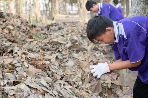Asian boy holds dry leaves which fall down to the ground in hands and pile them together to make composting fertilizer with his friends at school, earth day and environment day around the world .