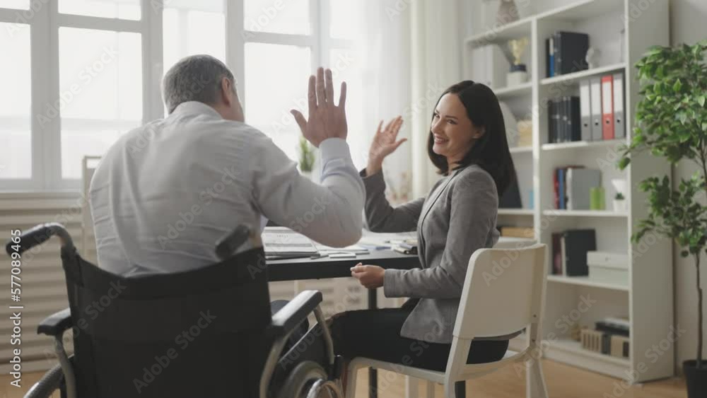 Businessman with disability giving high five to colleague, teamwork in office Businessman with disability giving high five to colleague, teamwork in office