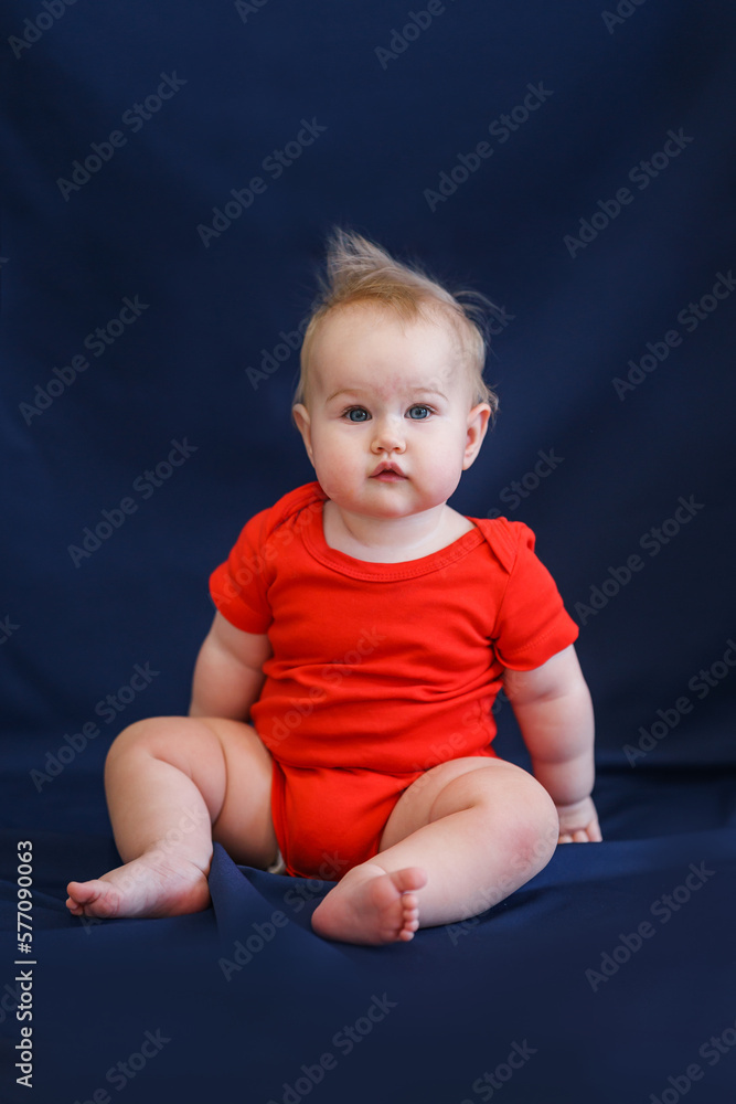 Charming caucasian baby toddler in a red bodysuit on a dark blue background Charming caucasian baby toddler in a red bodysuit on a dark blue background