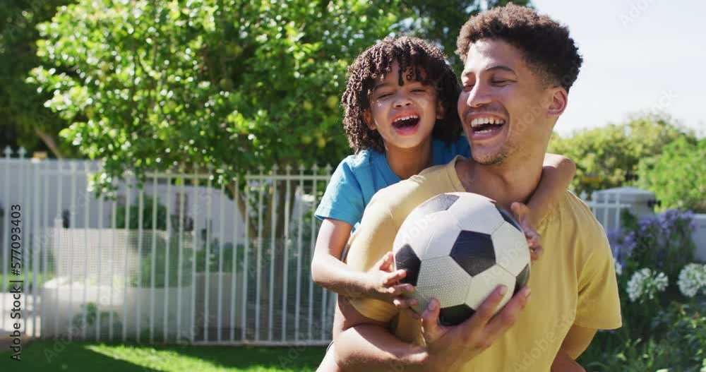 Portrait of happy biracial man and his son playing football in garden Portrait of happy biracial man and his son playing football in garden