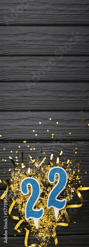 Number 22 blue celebration candle and gold confetti on dark wooden background. 22th birthday card. Anniversary and birthday concept. Vertical banner. photo