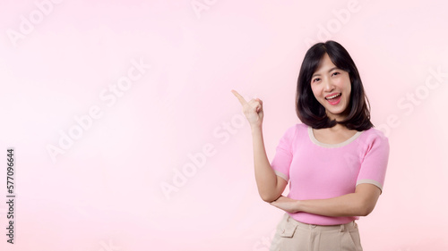 Portrait young beautiful asian woman happy smile pointing finger and hand to showing on copy space isolated on pink background. Attractive female person gesture attention to this promotion. © Jirawatfoto