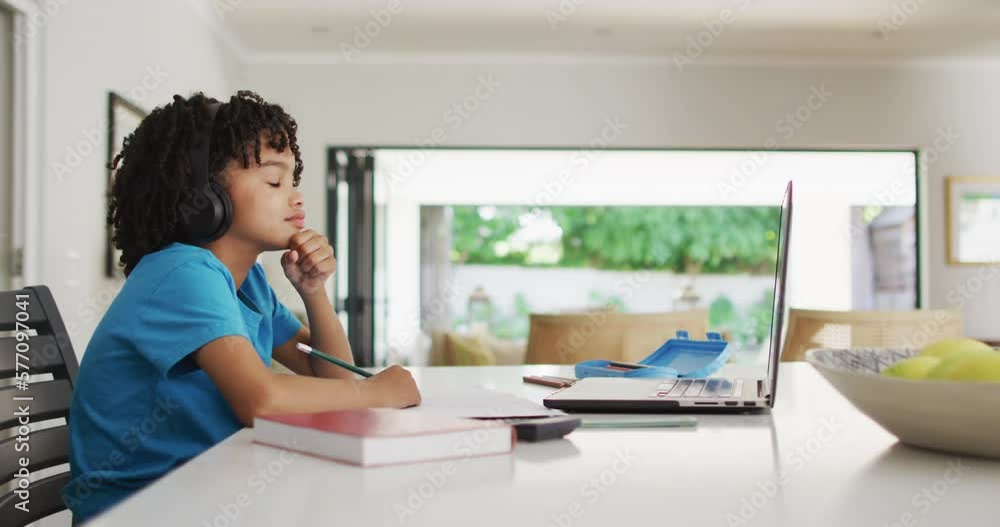 Happy biracial boy sitting at table using laptop and having online classes Happy biracial boy sitting at table using laptop and having online classes