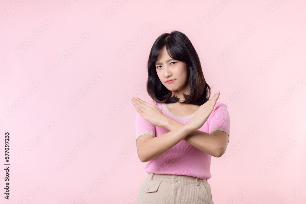 portrait serious young asian woman with cross arm gesture showing stop, no, wrong, denial, rejection sign isolated on pink pastel studio background. deny and negative expression symbol concept. portrait serious young asian woman with cross arm gesture showing stop, no, wrong, denial, rejection sign isolated on pink pastel studio background. deny and negative expression symbol concept.