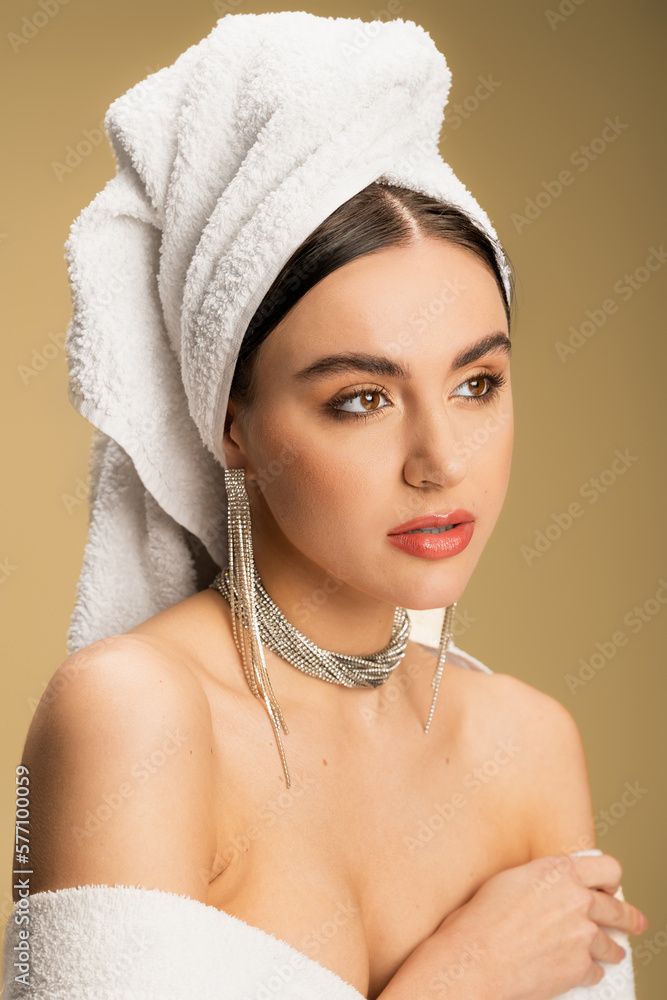 Fototapeta premium young woman in luxurious jewelry posing with towel on head on beige.