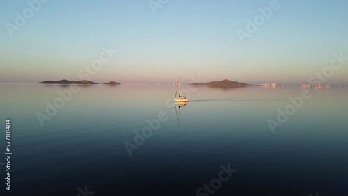 A boat crosses the Mar Menor at sunset. The sea is like a mirror and reflects the image of the boat, the blue sky and the islands. Sense of tranquility, peace and harmony. La Manga, Murcia, Spain